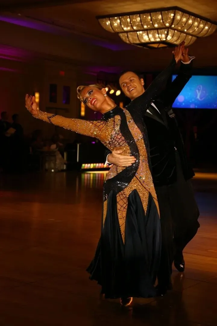 Slawek and Denise in a dramatic ballroom pose under a chandelier, Denise in a gold and black gown